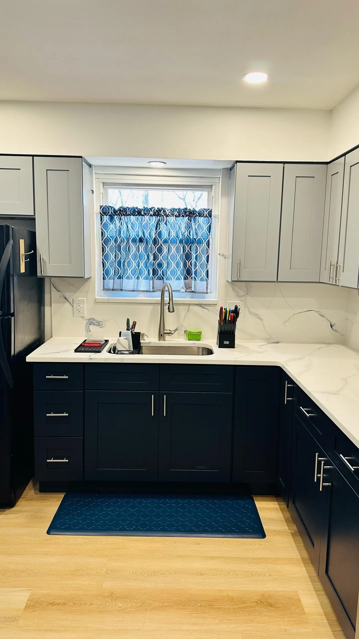 Kitchen remodel with two-tone navy and gray shaker cabinets, white quartz countertops, an undermount sink and light wood-look flooring.