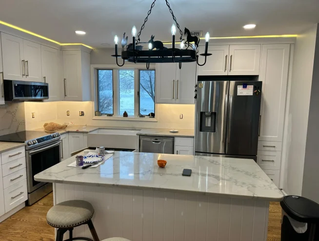 Kitchen remodel in Easton, PA with white shaker cabinets, a quartz island, stainless steel appliances and a wrought-iron chandelier.
